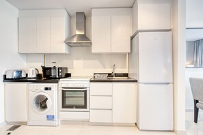 Uma cozinha moderna com armários brancos, coifa de aço inoxidável, forno embutido, máquina de lavar e geladeira.