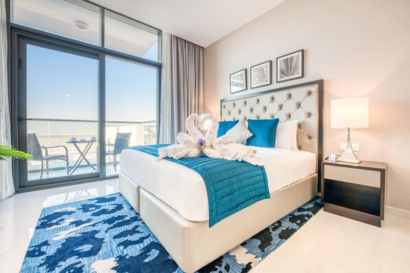 Quarto de hotel com uma cama grande, uma mesa de cabeceira, uma janela com vista e um tapete azul estampado.