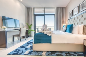 A modern hotel room with a large bed, a desk, a flat-screen TV, and a view of the city through large windows.