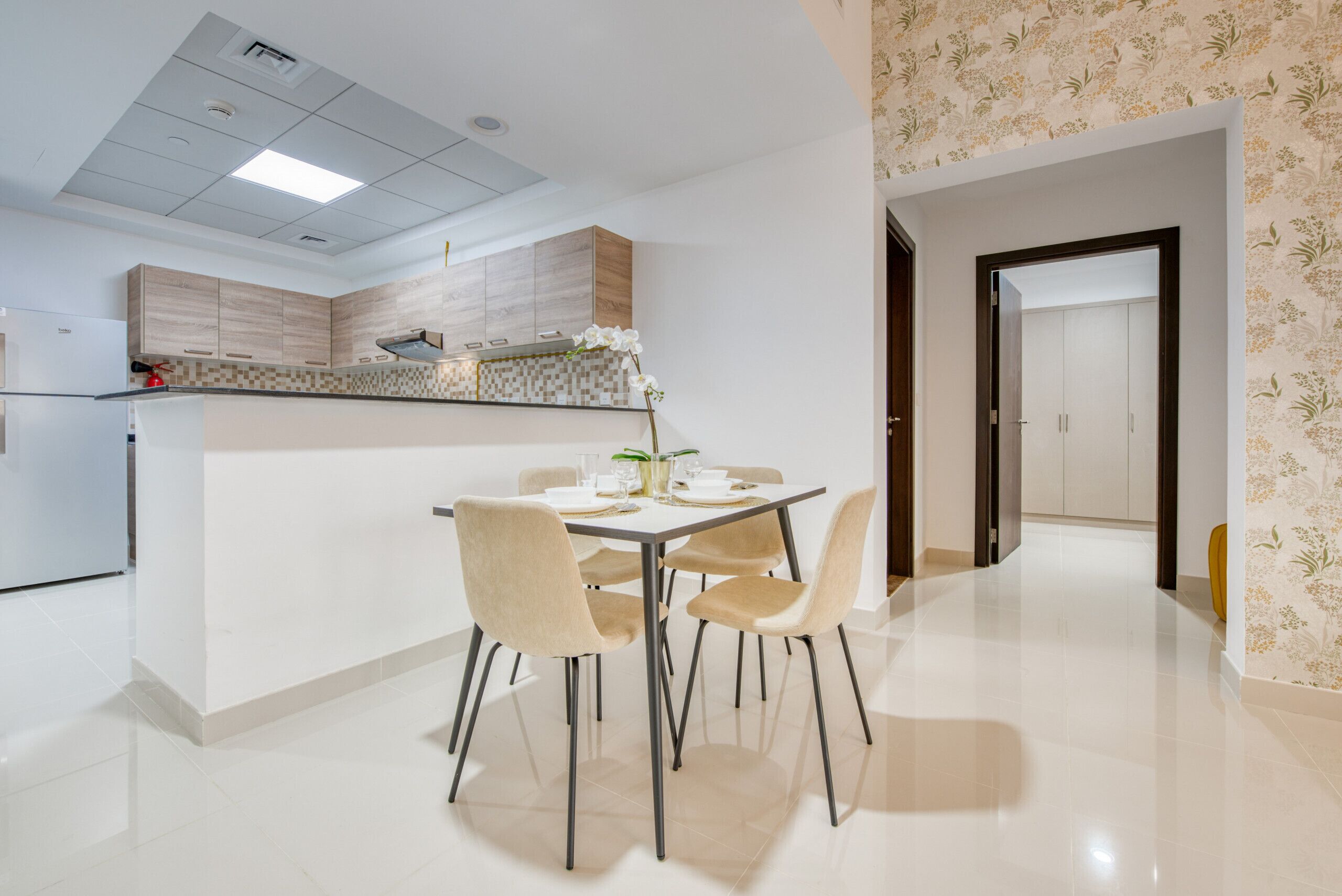 Une cuisine moderne dotée d’un îlot central, d’un coin repas avec quatre chaises et d’un couloir menant à une porte.