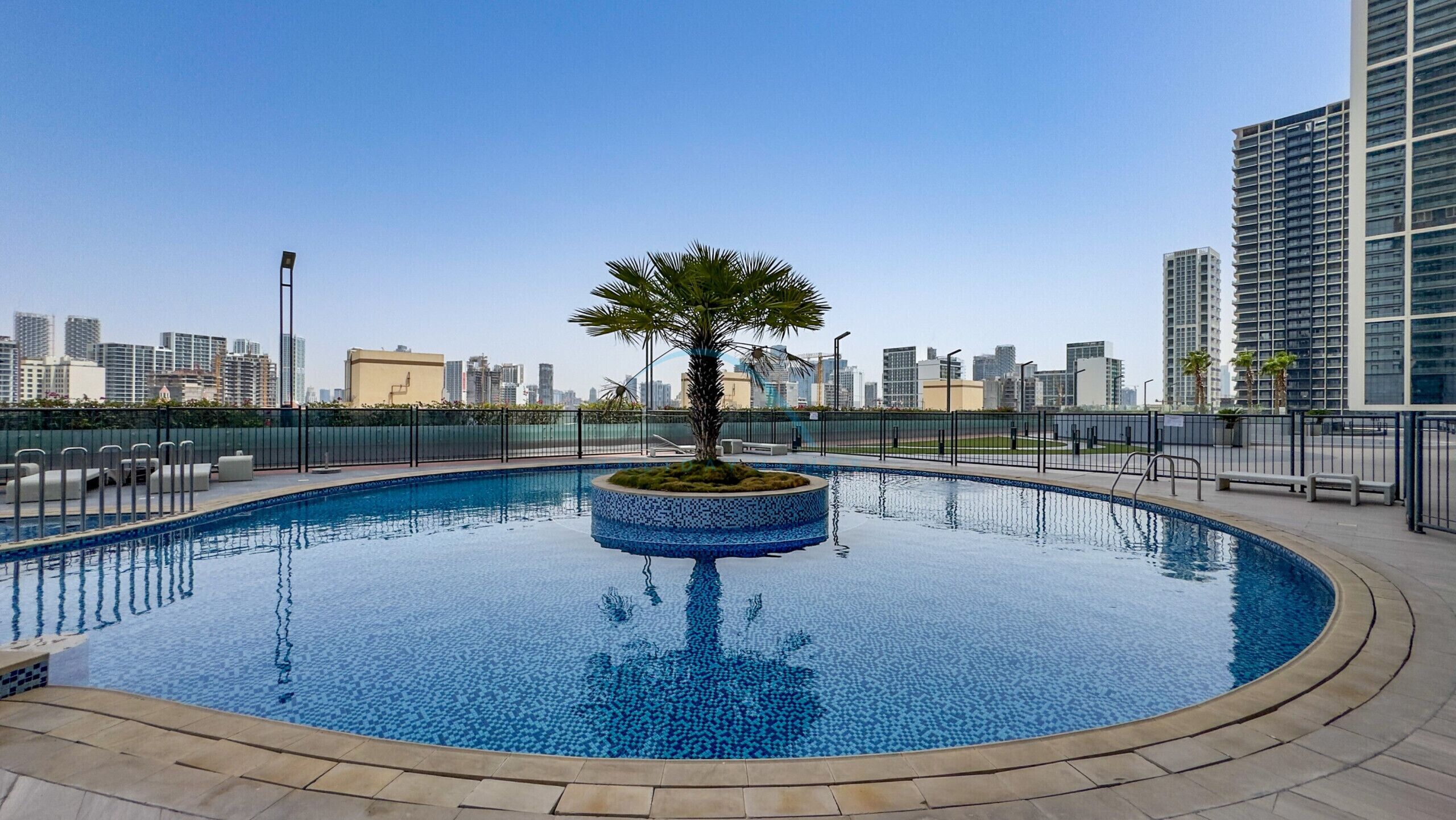 A rooftop pool with a palm tree, surrounded by high-rise buildings.