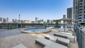 A rooftop pool with lounge chairs and a city skyline in the background. - Sky-High Studio, Few Minutes Walk from Circle Mall and Near the Park (Dubai)