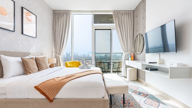A modern hotel room with a large bed, a TV, a balcony with a city view, and a desk with a chair. - Sky-High Studio, Few Minutes Walk from Circle Mall and Near the Park (Dubai)