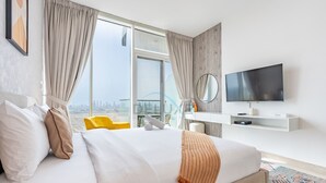 A hotel room with a large bed, a TV, a view of the city, and a balcony with yellow chairs. - Sky-High Studio, Few Minutes Walk from Circle Mall and Near the Park (Dubai)