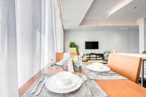 Un espace repas moderne avec une table dressée pour deux personnes, un téléviseur en arrière-plan et une plante sur la table.