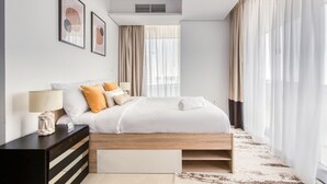 Quarto moderno com cama de madeira, roupa de cama branca e mesa de cabeceira com abajur.