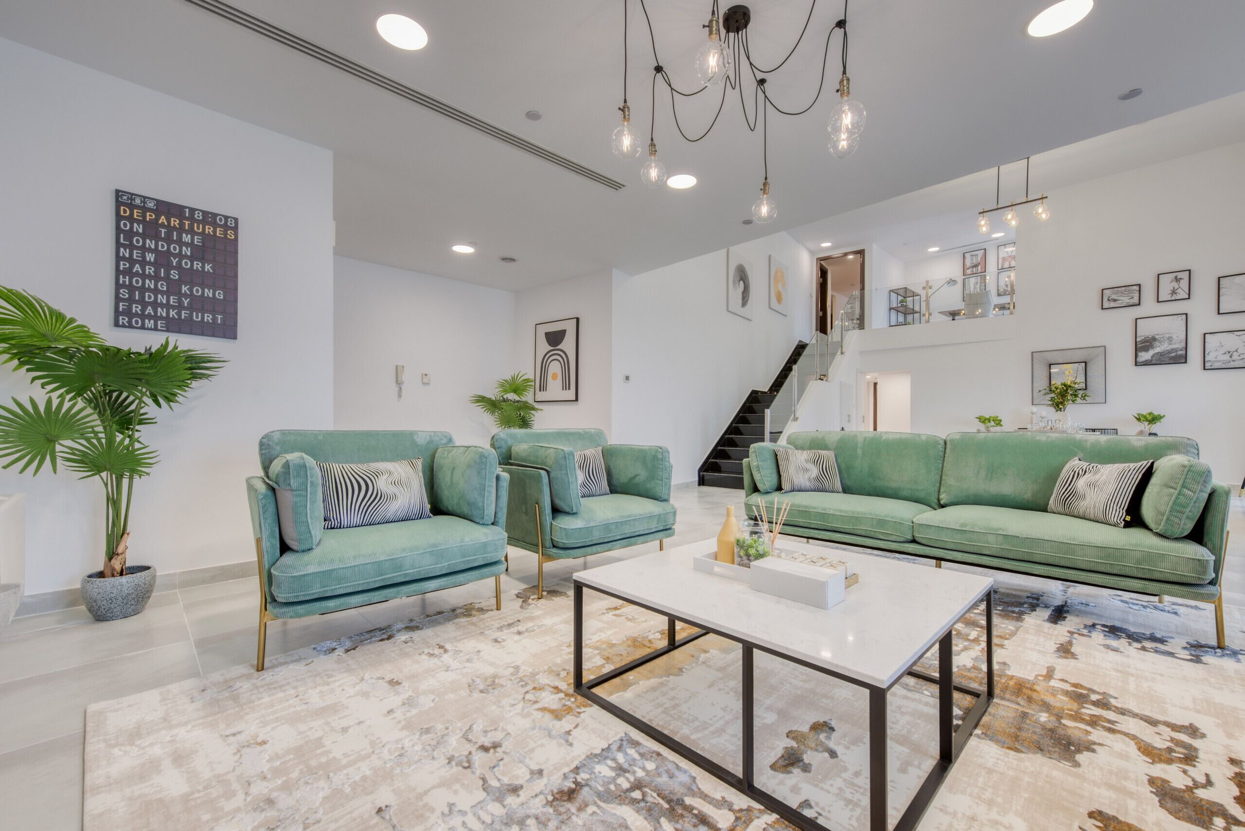 A modern living room with two teal sofas, a white coffee table, and a staircase leading to an upper level.