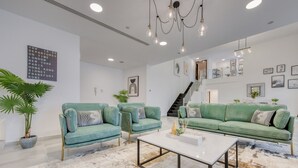 A modern living room with two teal sofas, a white coffee table, and a staircase leading to an upper level. - Outstanding 3BR at Sadaf 7 JBR by Deluxe Holiday Homes (Dubai)