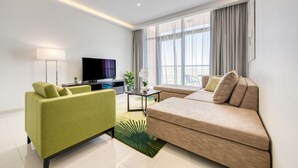 A modern living room with a green sofa, beige sofa, flat-screen TV, and large windows with curtains. - Luxury 1BR at DAMAC Celestia A Dubai South by Deluxe Holiday Homes (Dubai)