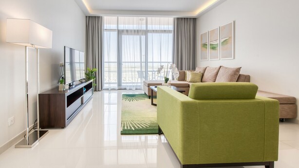 A modern living room with a green sofa, a flat-screen TV, and a large window with curtains. - Luxury 1BR at DAMAC Celestia A Dubai South by Deluxe Holiday Homes (Dubai)