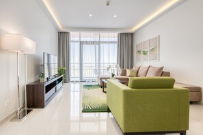 Uma sala de estar moderna com um sofá verde, uma televisão de tela plana e uma janela grande com cortinas.