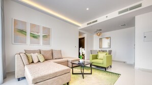 A modern living room with a beige sofa, a green armchair, and a coffee table. There are three framed artworks on the wall and a mirror above the armchair. - Luxury 1BR at DAMAC Celestia A Dubai South by Deluxe Holiday Homes (Dubai)