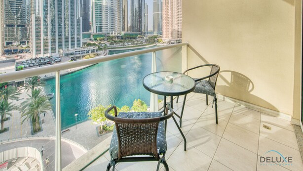 A balcony with a glass table and wicker chairs overlooking a marina with tall buildings in the background.