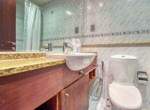 Een badkamer met een marmeren wand, een wastafel met kraan, toilet en een douche.