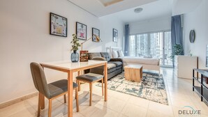 A modern living room with a dining table, sofa, and a view of the city through large windows.