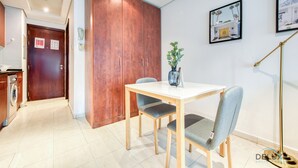 A modern hotel room with a wooden wardrobe, a dining table with two chairs, a potted plant, and a framed picture on the wall.