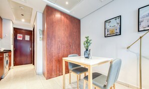 Une chambre d’hôtel moderne avec une armoire en bois, une table à manger avec deux chaises, une plante en pot et un tableau encadré au mur.