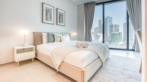 Un dormitorio moderno con una cama grande, dos mesitas de noche y vistas a la ciudad a través de ventanales de piso a techo.