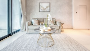 Una sala de estar moderna con una mesa de centro redonda de mármol, un sofá color beige y un ventanal con cortinas traslúcidas.