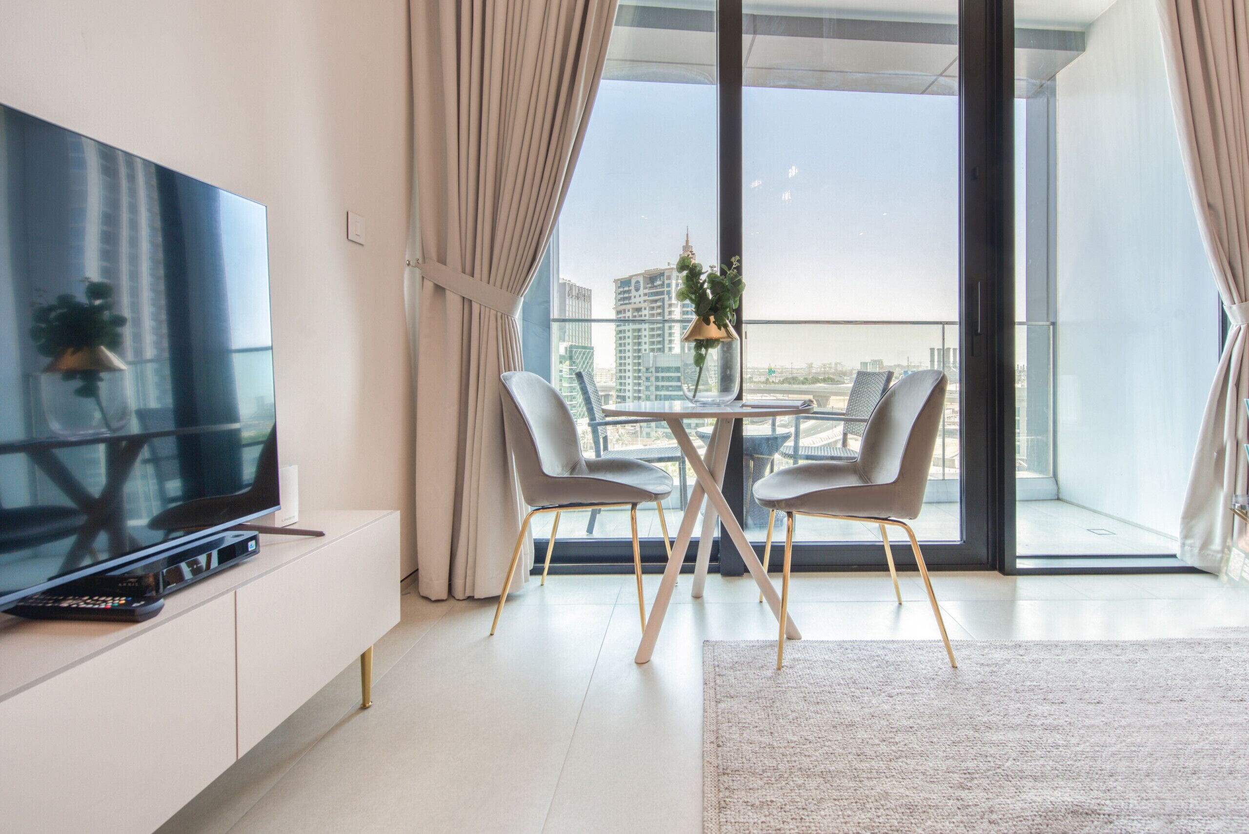 Un soggiorno moderno con una televisione a schermo piatto, un tavolo da pranzo con sedie e un'ampia finestra vista sullo skyline della città.