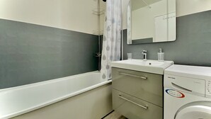 Ein modernes Badezimmer mit Badewanne, Waschbecken, Spiegel und Waschmaschine.