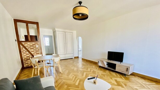 Ein modernes Wohnzimmer mit einer Couch, einem Fernseher und einem Essbereich mit Stühlen und einem Tisch.