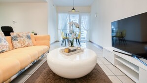 Un soggiorno moderno con divano, poggiapiedi, TV e zona pranzo con sedie e tavolo.