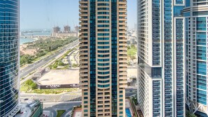 Un edificio alto con facciata curva, circondato da altri grattacieli, cielo sereno e vista lontana su un ponte e sull'acqua.