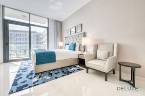 Quarto de hotel moderno com uma cama grande, área de estar e vista para a cidade através de janelas do chão ao teto.
