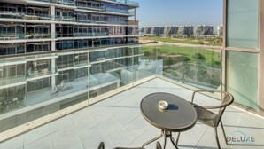 Een balkon met glazen hekwerk, een ronde tafel en een rieten stoel. Achtergrond met moderne gebouwen en een heldere lucht.