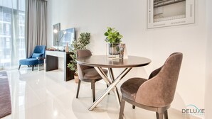 Een moderne woonkamer met een ronde tafel, twee stoelen, een blauwe fauteuil, een bureau en een potplant.