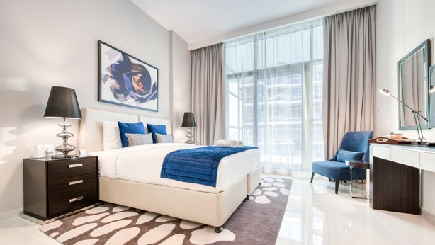Een moderne hotelkamer met een groot bed, een bureau, een stoel en een groot raam met gordijnen.
