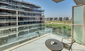 Un balcon doté d’une balustrade en verre, une table ronde et un fauteuil en osier. En arrière-plan, on aperçoit des bâtiments modernes et un ciel dégagé.