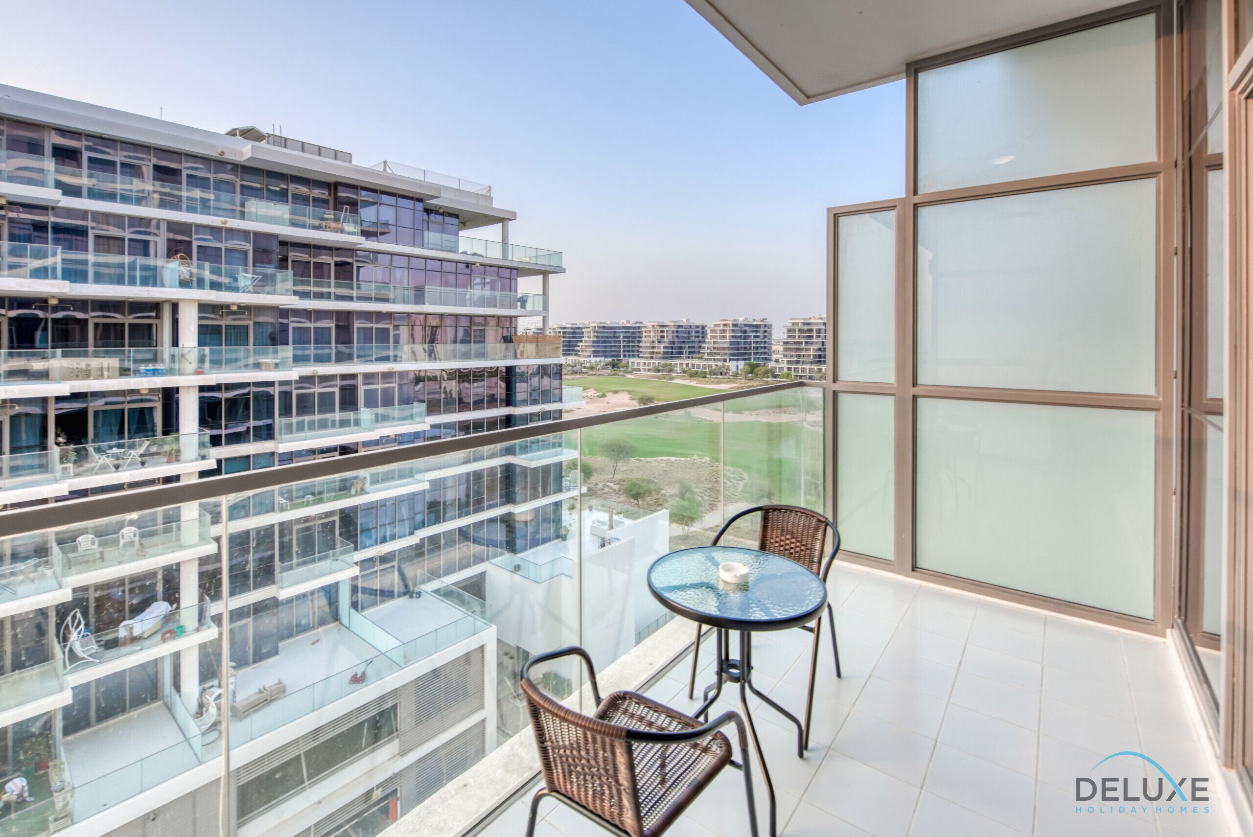 Eine moderne Wohnung mit Balkon, ausgestattet mit Glastrennwand, zwei Korbstühlen und einem kleinen Tisch.