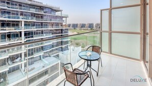 A modern apartment with a balcony featuring a glass railing, two wicker chairs, and a small table.