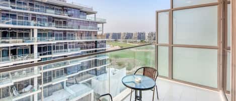 Un appartement moderne doté d’un balcon avec une balustrade en verre, deux fauteuils en osier et une petite table.
