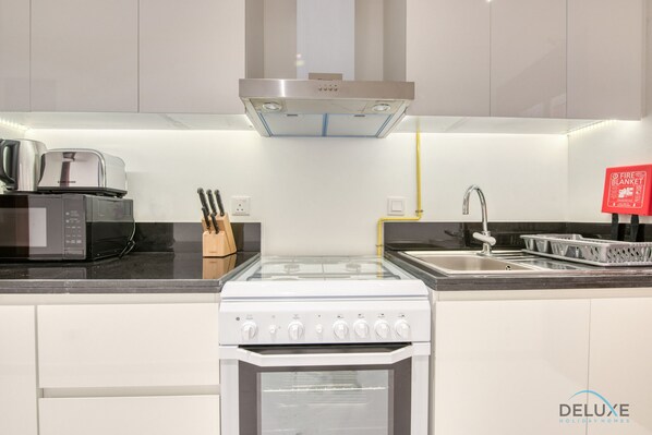 A modern kitchen with a built-in oven, microwave, and stove. There is a knife block, a sink, and a fire blanket sign. - Stunning Studio at Golf Promenade 2A Damac Hills by Deluxe Holiday Homes (Dubai)