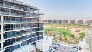 A modern multi-story building with a glass facade, a parking area, and a view of a golf course.