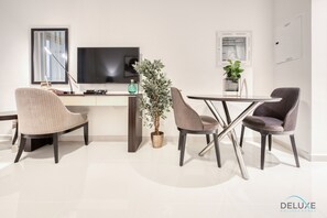 Un salon moderne avec un téléviseur à écran plat, deux fauteuils, une table basse et une plante en pot.