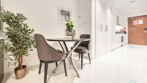 A modern dining area with a round table and four chairs, a potted plant, and a kitchen in the background.