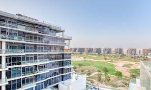 A modern multi-story building with a glass facade, a parking area, and a view of a golf course.