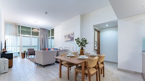 A modern living room with a dining area, featuring a sofa, a dining table set for four, and a large window with curtains. - Huge Balcony Overlooking Creek Harbour with Glimpses of Burj Khalifa (Dubai)