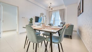 A modern dining area with a rectangular table, grey upholstered chairs, and a chandelier.