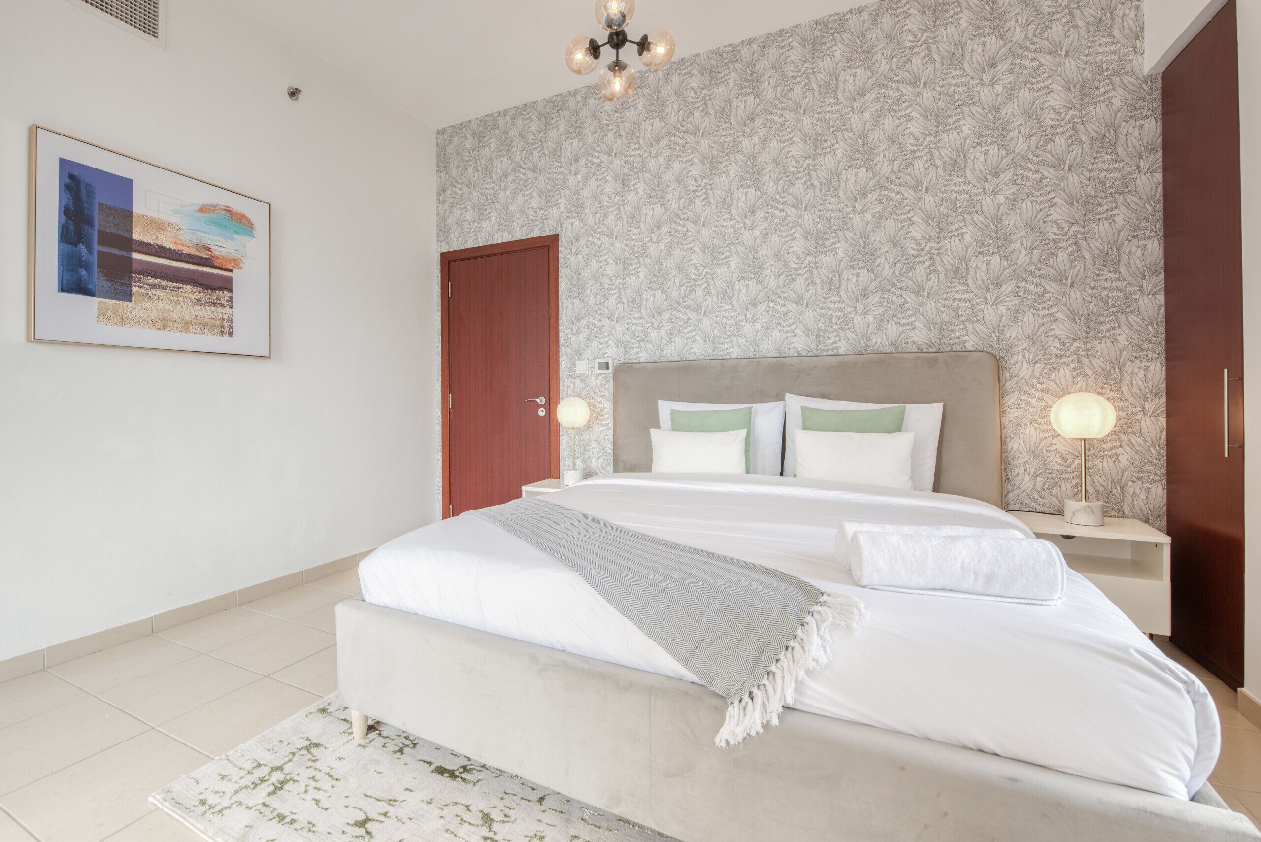 Une chambre à coucher avec un grand lit, une tête de lit dotée de lampes, une porte et un papier peint à motifs.