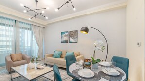 A modern living room with a dining area, featuring a sofa, a coffee table, and a dining table set with plates and glasses. - Dazzling 1BR at Marina Crown Dubai Marina by Deluxe Holiday Homes (Dubai)