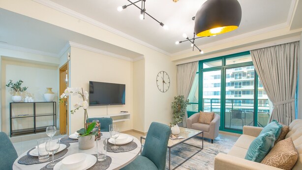 A modern living room with a dining area, a flat-screen TV, and a large window with curtains. - Dazzling 1BR at Marina Crown Dubai Marina by Deluxe Holiday Homes (Dubai)