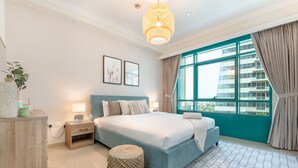 A modern bedroom with a large bed, a bedside table, a lamp, a small round ottoman, and a view of a building through a large window. - Dazzling 1BR at Marina Crown Dubai Marina by Deluxe Holiday Homes (Dubai)