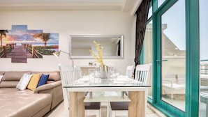 Un salón moderno con una mesa de comedor de cristal, un sofá beige y un ventanal con vistas a la ciudad.