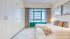 Un dormitorio con una cama grande, un armario, una ventana con cortinas y obras de arte en la pared.