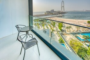A balcony with a glass railing overlooking a beach, pool, and a Ferris wheel.